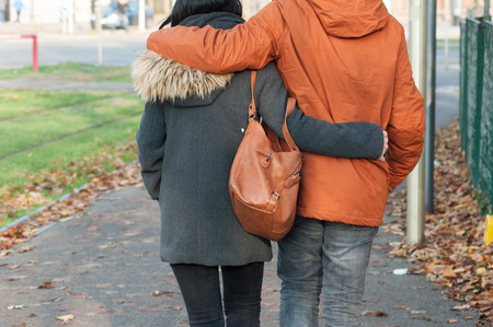 closeup of couple back entwined walking in the street by autumnの写真素材