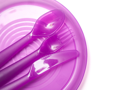 closeup of plastic plate, fork, knife and purple spoon on white backgroundの写真素材