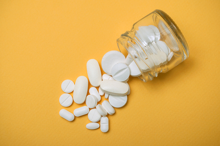 closeup of white pils falling from glass container on yellow backgroundの写真素材