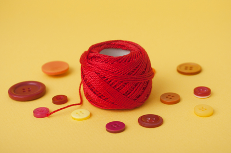 closeup of red string bobbin and plastic buttons on yellow background