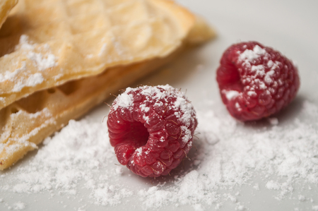 closeup of raspberries with sugar on waffle in shaped heart background on a white plateの写真素材