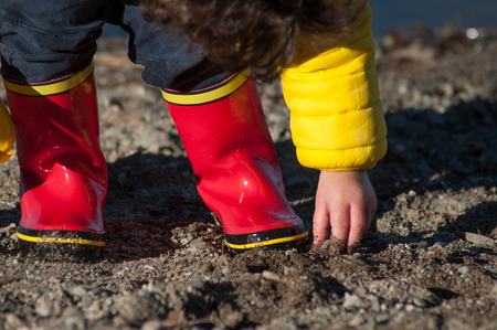 closeup of boy  playing with pebbles in border the lake wearing rubber boots