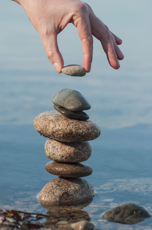 Closeup of man putting pebble on stone balance  in the water of lake with reflectionの写真素材