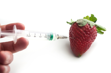 closeup of hand of man injecting with a syringe into a strawberry on white backgroundの写真素材