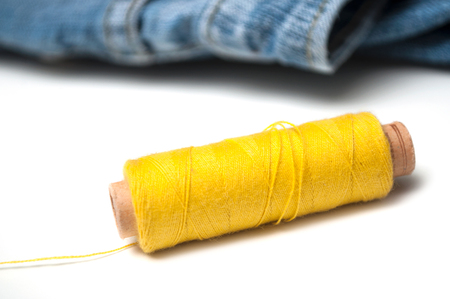 closeup of yellow sewing thread spool bobbin on white table on blue jeans background