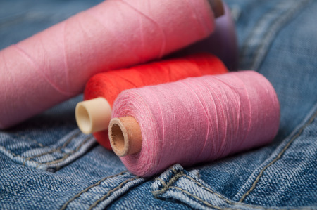 closeup of colorful sewing thread spool bobbins on blue jeans background