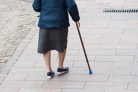 closeup of aged woman walking with stick in the street  on back viewの写真素材