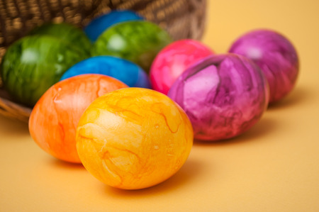 closeup of decorative painted easter eggs falling from wooden basket on yellow background