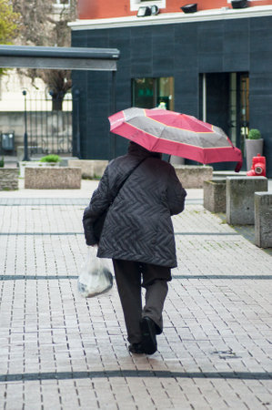 Mulhouse - France - 3 April 2019 -  portrait of old woman with pink umbrella and grey coat in the street on back viewのeditorial素材