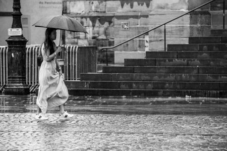 Mulhouse - France - 28 May 2019 - portrait of woman wearing with a dress walking with umbrella on cobbles place in the cityのeditorial素材