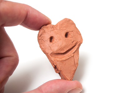 Closeup of terra cotta smiley in shaped  heart  in hand on white backgroundの写真素材