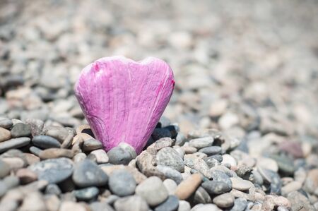 Closeup of pink painting on stone pebble in shaped heart on pebble beach