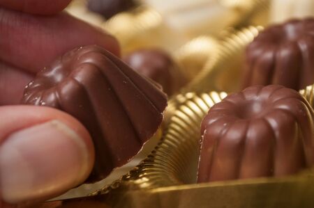 Closeup of hand of man taking a Chocolate in shaped kouglofs in golden box collectionの写真素材