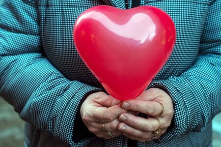 Closeup of red inflatable balloon in shaped heart in hands of woman in the streetの写真素材