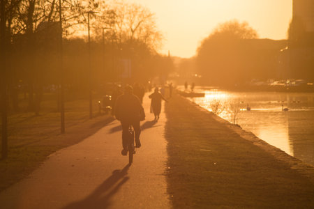 Mulhouse - France - 16 January 2020 -  Silhouettes of people with bicycle in border river by sunsetのeditorial素材