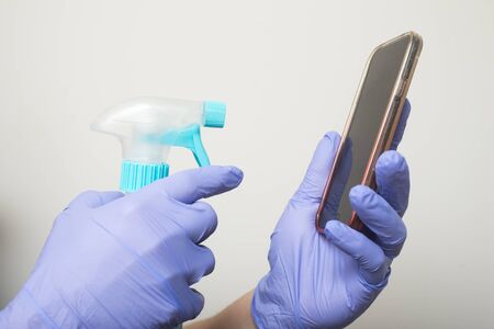 Closeup of hands wearing latex gloves for cleaning the screen of her smartphone on white background to protect against the coronavirus pandemic の写真素材