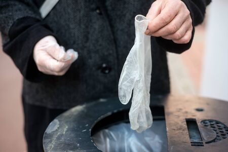 Closeup of hands of woman putting used latex gloves in the garbage in the street 