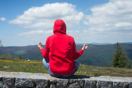 Portrait on back view of man sitting on stoned wall mediting and looking the mountain landscapeの写真素材