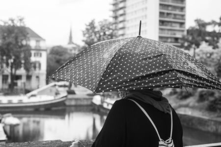 Portrait of woman standing in the street with black umbrella on back viewの写真素材