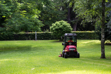 municipal employee driving Red tractor and lawn mower, shears lawns in urban parkのeditorial素材