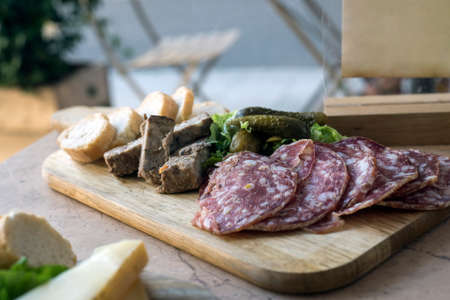 Closeup of slices of saussage and bread on a wooden cutting board on the table at the restaurant terraceの写真素材