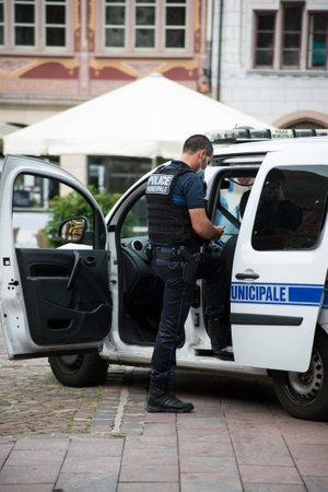 Mulhouse - France - 22 August 2020 - Portrait of municipal policeman at phone and police car on the main placeのeditorial素材