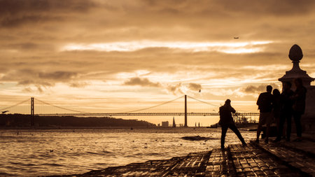 silhouette of tourist taking a picture of the famous 25th April suspension bridge on sunset...