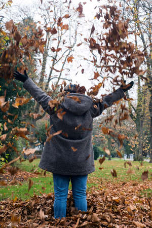 Portrait on back view of woman playing with autumnal leaves in a public garden