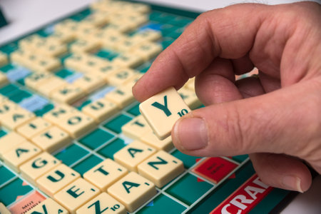 Mulhouse - France - 16 November 2020 - Closeup of hand of woman playing with plastic letter Y to forming a word on Scrabble board gameのeditorial素材