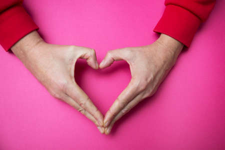 Closeup of hands of man in sheped heart on pink backgroundの写真素材
