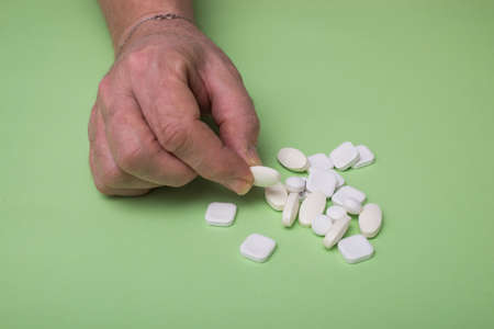 Closeup of woman taking drug pills in hand on green background