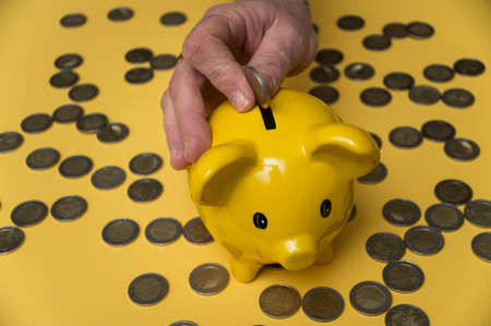 Closeup of hands of woman insert one euro coin in her yellow piggy bank on yellow background