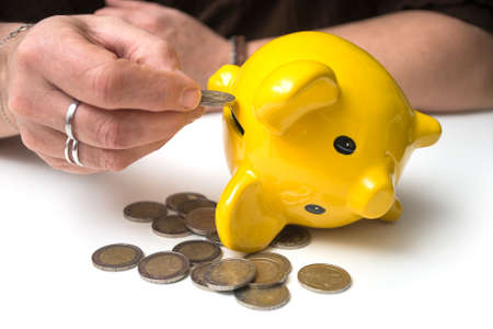 Closeup of hands of woman insert one euro coin in her yellow piggy bank on white background