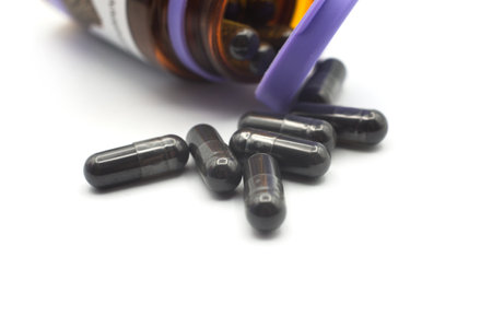 Closeup of black capsules of coal falline from a glass container on white backgroundの写真素材