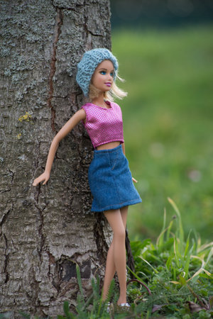 Mulhouse - France - 4 march 2021 - Portrait of blond Barbie doll with woolen hat and blue jeans skirt standing in a public garden against a tree trunkのeditorial素材