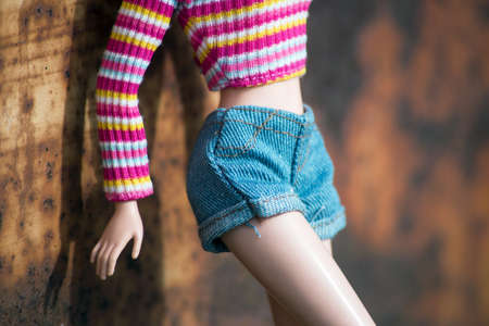 Closeup of mannequin doll with a colorful stripped top and blue jeans short standing against a rusty door in the streetの写真素材