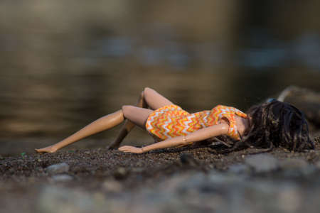 Portrait of mannequin doll lying on the sand in border river with her orange summer dressの写真素材