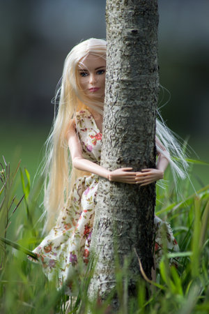 Mulhouse - France - 10 April 2021 - Portrait of blond Barbie doll wearing a printed flowers summer dress hugging tree in the forestのeditorial素材