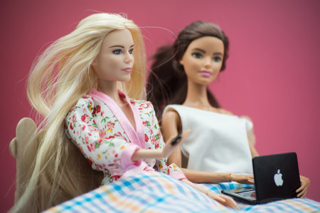 Mulhouse - France - 16 April 2021 - Portrait of blond and brunette barbie dolls sitting in the bed with a apple computer on pink backgroundのeditorial素材