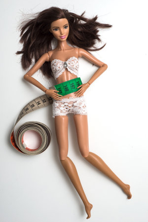 Mulhouse - France - 22 April 2021 - Portrait of brunette Barbie doll wrapped in measuring tape on white background, female fight for a perfect body - Dieting conceptのeditorial素材