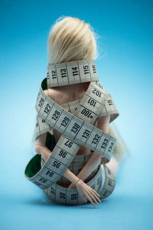 Closeup of Doll wrapped in measuring tape on blue background -  female fight for a perfect body -...