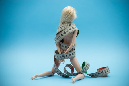 Closeup of Doll wrapped in measuring tape on blue background -  female fight for a perfect body - Dieting conceptの写真素材