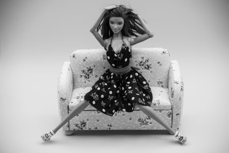 Mulhouse - France - 1 st june 2021 - Portrait of brunette barbie doll wearing a black summer dress sitting on sofa in black and whiteのeditorial素材