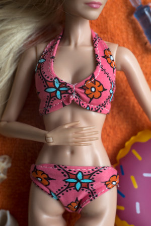Closeup of blond mannequin doll wearing a colorful bikini lying on orange bath towel with accessoriesの写真素材