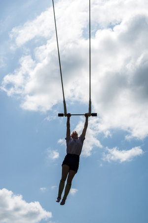 Mulhouse - France - 18 July 2021 - Portrait of girl balancing on trapeze during the street scene festival pn blue cloudy sky backgroundのeditorial素材