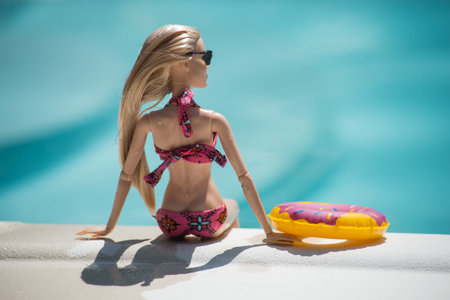 Mulhouse - France - 21 July 2021 - Portrait of blond barbie doll wearing a pink bikini and sunglasses sitting in border the swimming pool by sunny dayのeditorial素材