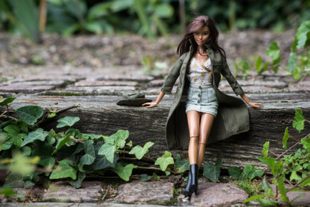 Mulhouse - France - 12 October 2021 - Portrait of brunette barbie doll wearing a blue jeans mini skirt and a green rain coat standing in a public gardenのeditorial素材