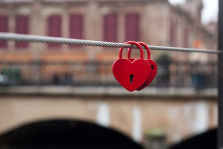 Closeup of two red padlocks in shaped heart on metallic cable in border waterの写真素材