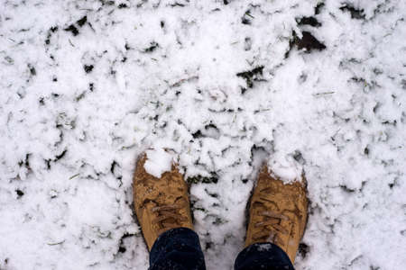 Closeup of feet of man wearing boots in the grass covered by the snowの写真素材