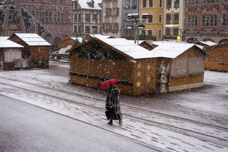 Mulhouse - France - 10 December 2021 - woman with a red umbrella walking at the christmas market by snowy dayのeditorial素材